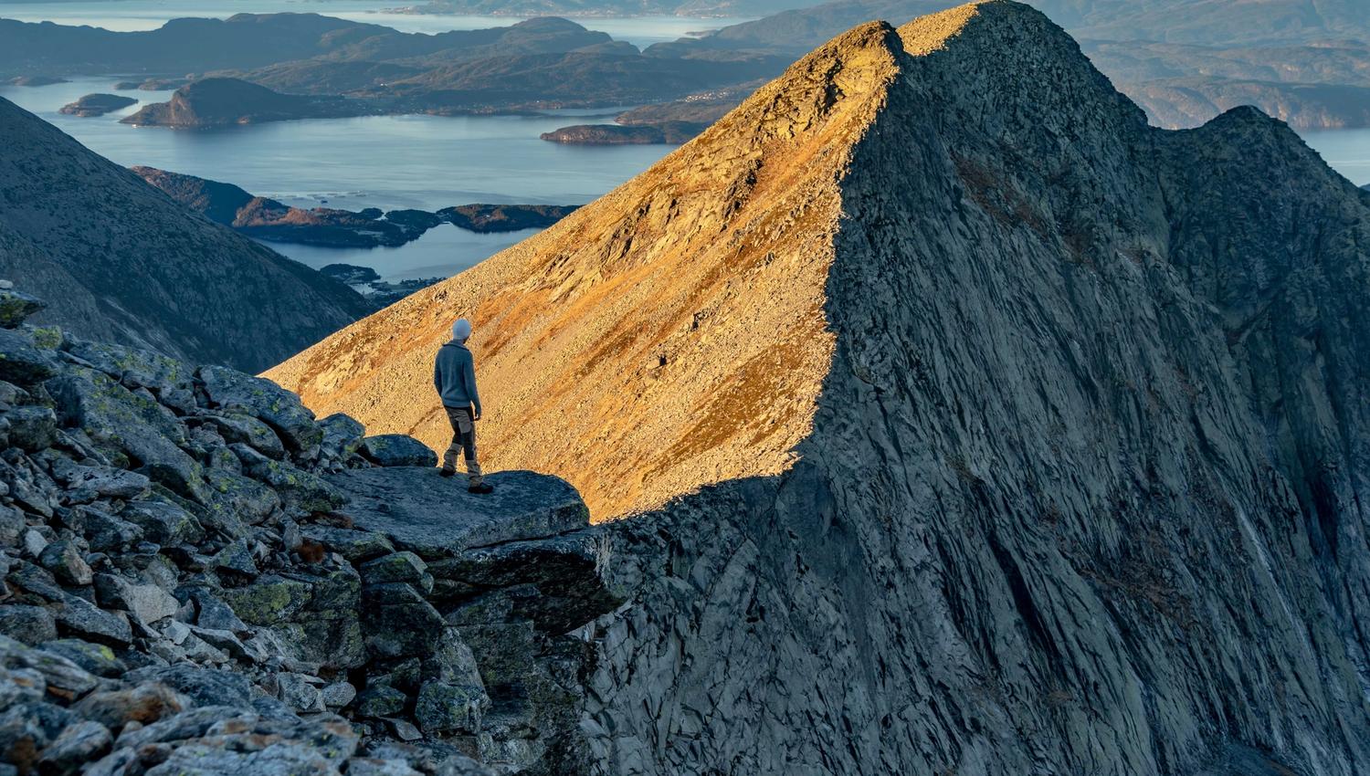 Hiker standing on the ridge of the Ulvanosa massif with sweeping views of mountains and fjords in Hardanger, on the trail from Uskedalen to Ulvanosa,