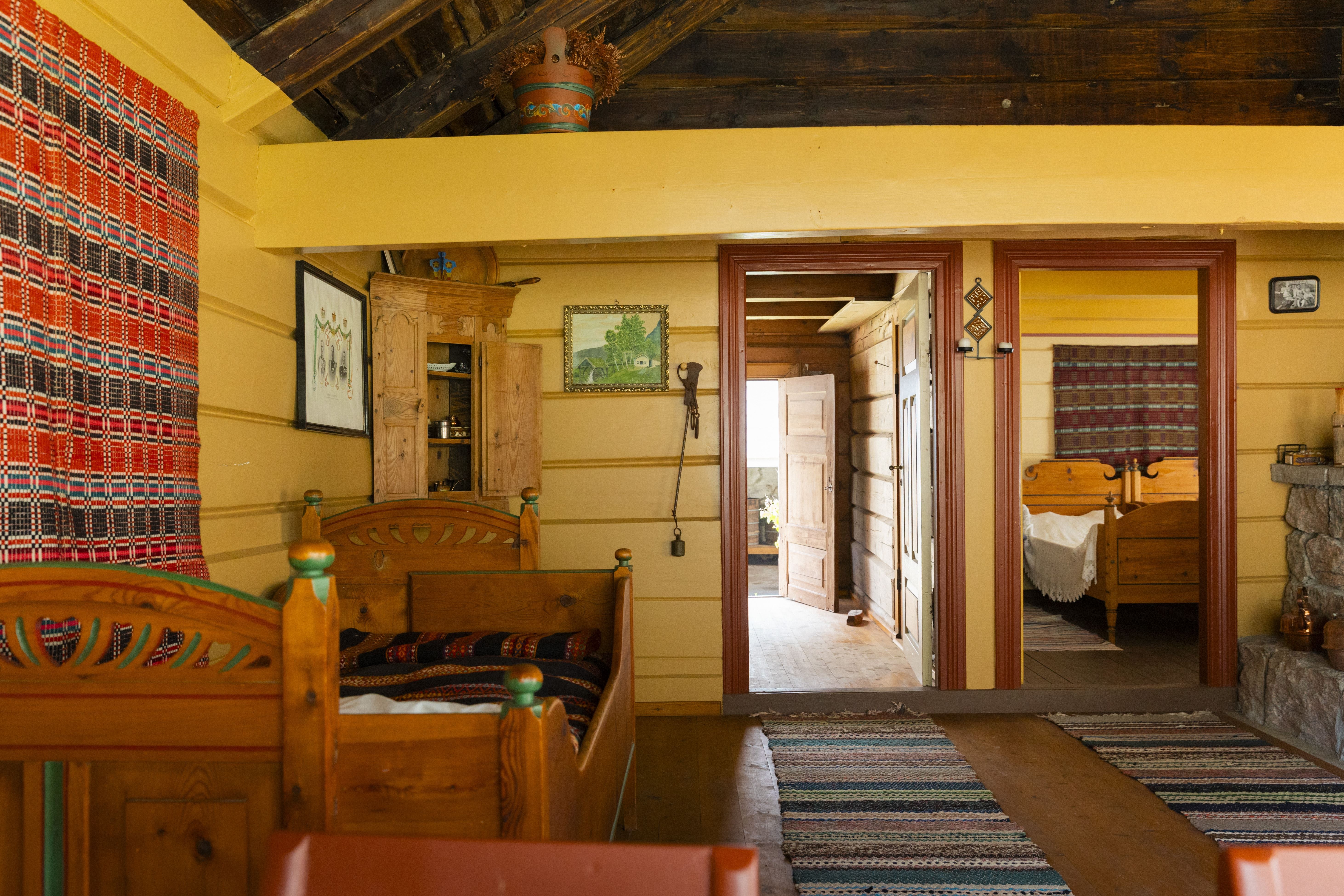 Rustic cabin room with wooden bed frames, striped textiles, wall art, rugs, and open doors to a bedroom.