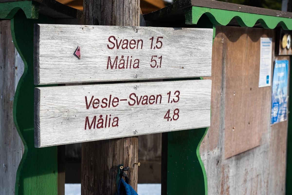 A wooden sign in a winter landscape showing distances to various destinations, mounted on a small building.