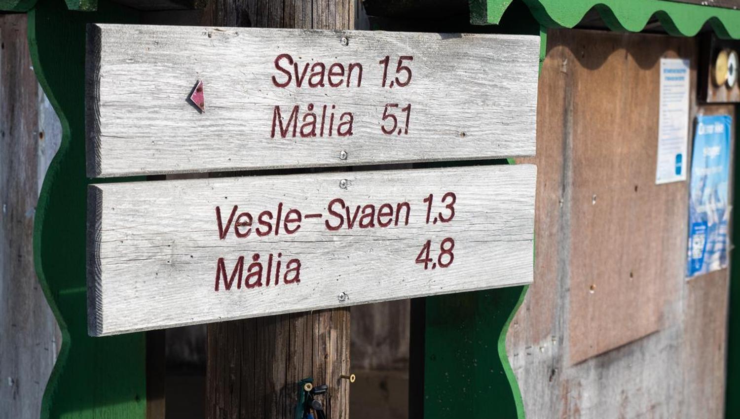 A wooden sign in a winter landscape showing distances to various destinations, mounted on a small building.