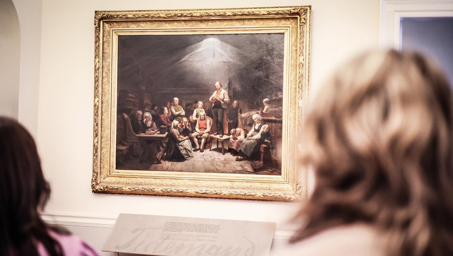 A couple is looking at the large painting ‘The Haugeans’ at the Mandal Museum, in which Adolph Tidemand depicts the followers of the lay preacher Hans