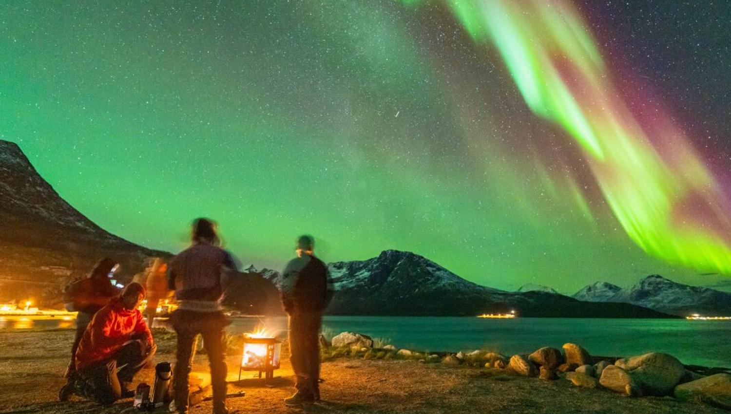 Guests sit by the fire and relax while the Northern Lights dance above