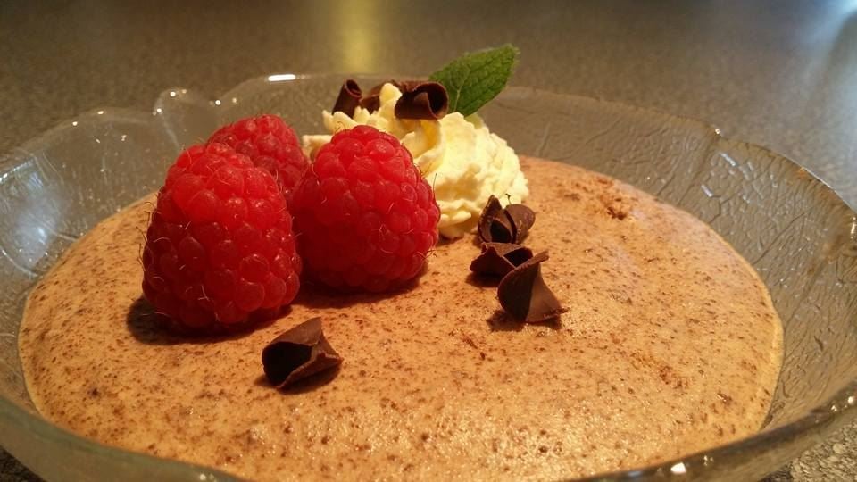 Close-up of chocolate mousse in a glass dish, topped with raspberries, whipped cream, mint, and chocolate curls.