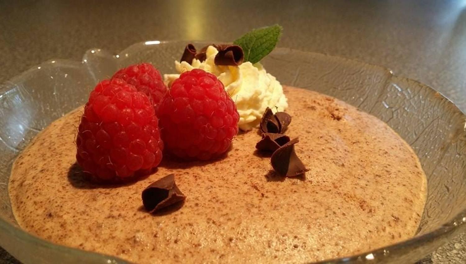 Close-up of chocolate mousse in a glass dish, topped with raspberries, whipped cream, mint, and chocolate curls.
