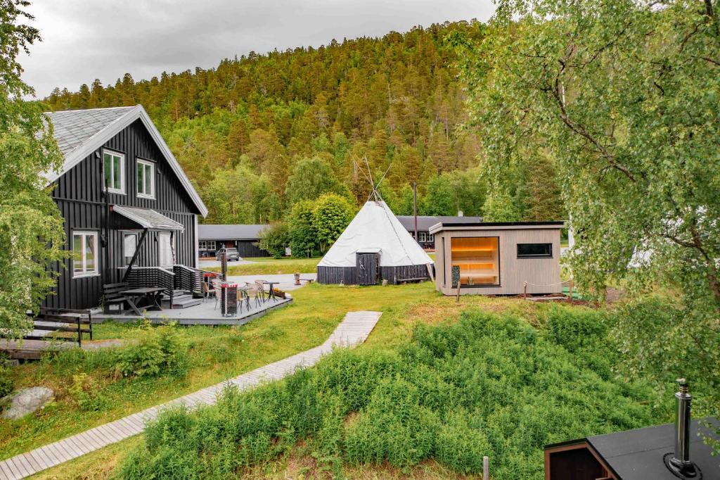 A scenic view of traditional black cabins, a tipi, and a modern structure amidst lush greenery.