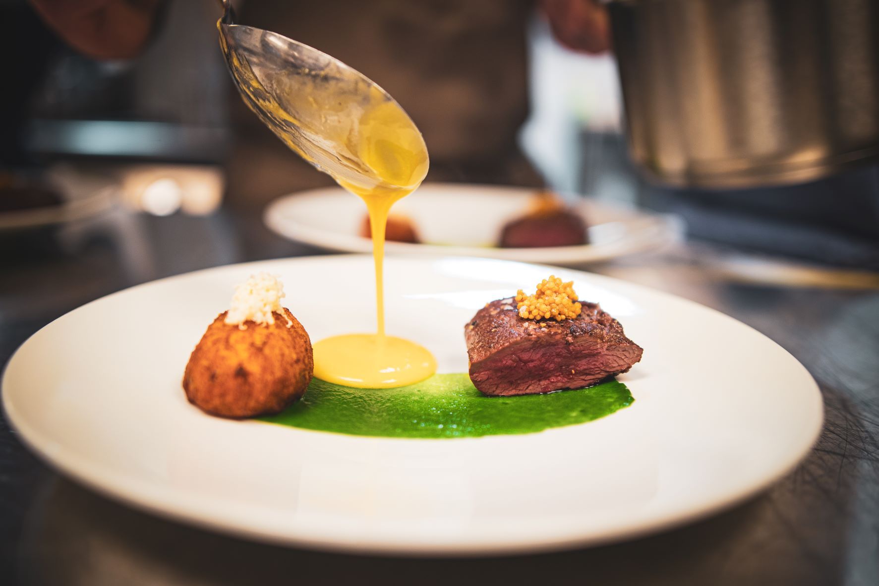 A food dish on which a chef is pouring sauce from a spoon