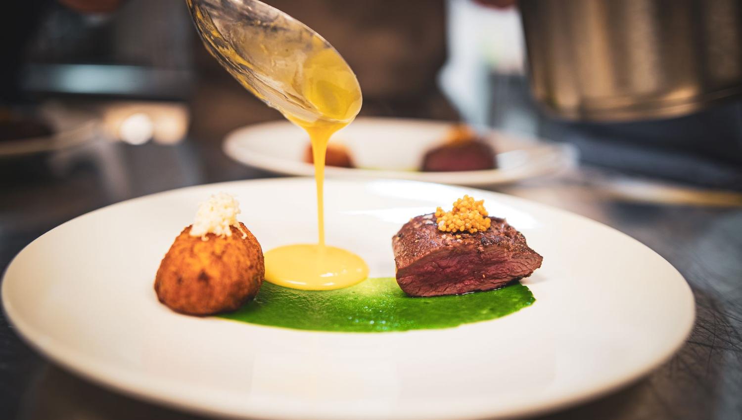 A food dish on which a chef is pouring sauce from a spoon