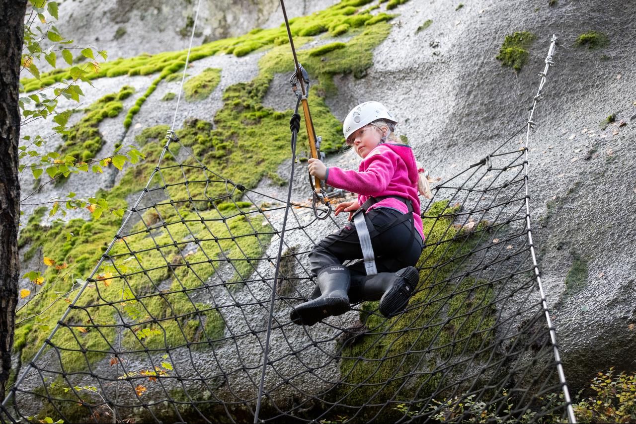 A child in the net attaches the safety hook to the line in order to progress on the climbing trail