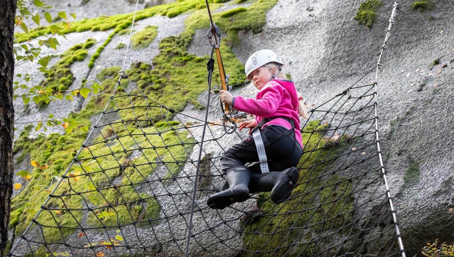 A child in the net attaches the safety hook to the line in order to progress on the climbing trail