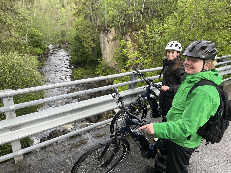 Syklistene står oppå brua og ser på elven
