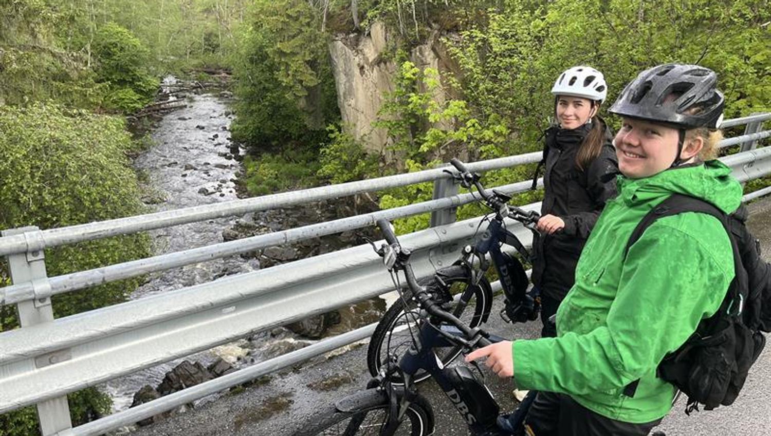 Syklistene står oppå brua og ser på elven