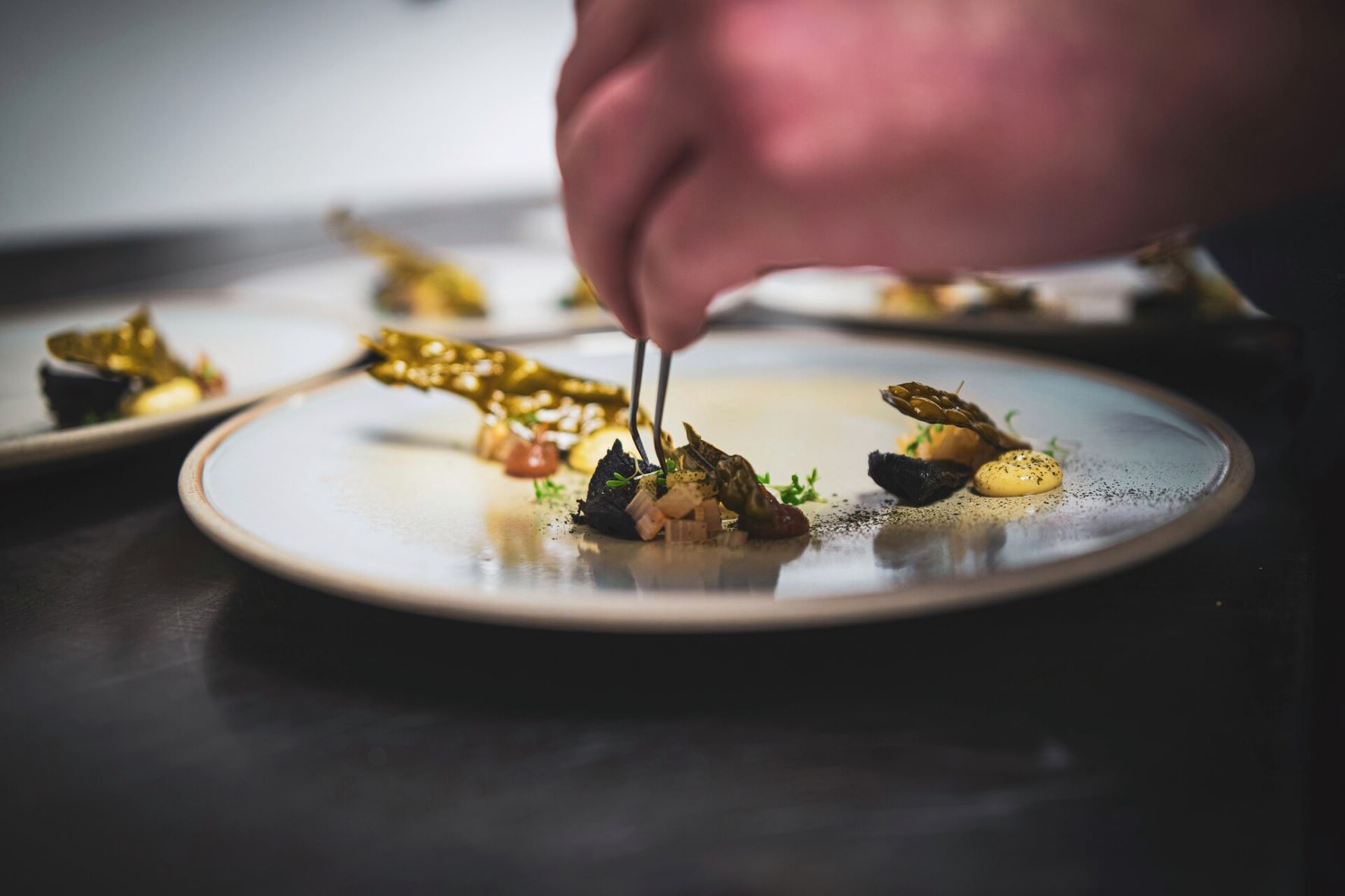 A chef preparing a dish on a plate with pincers
