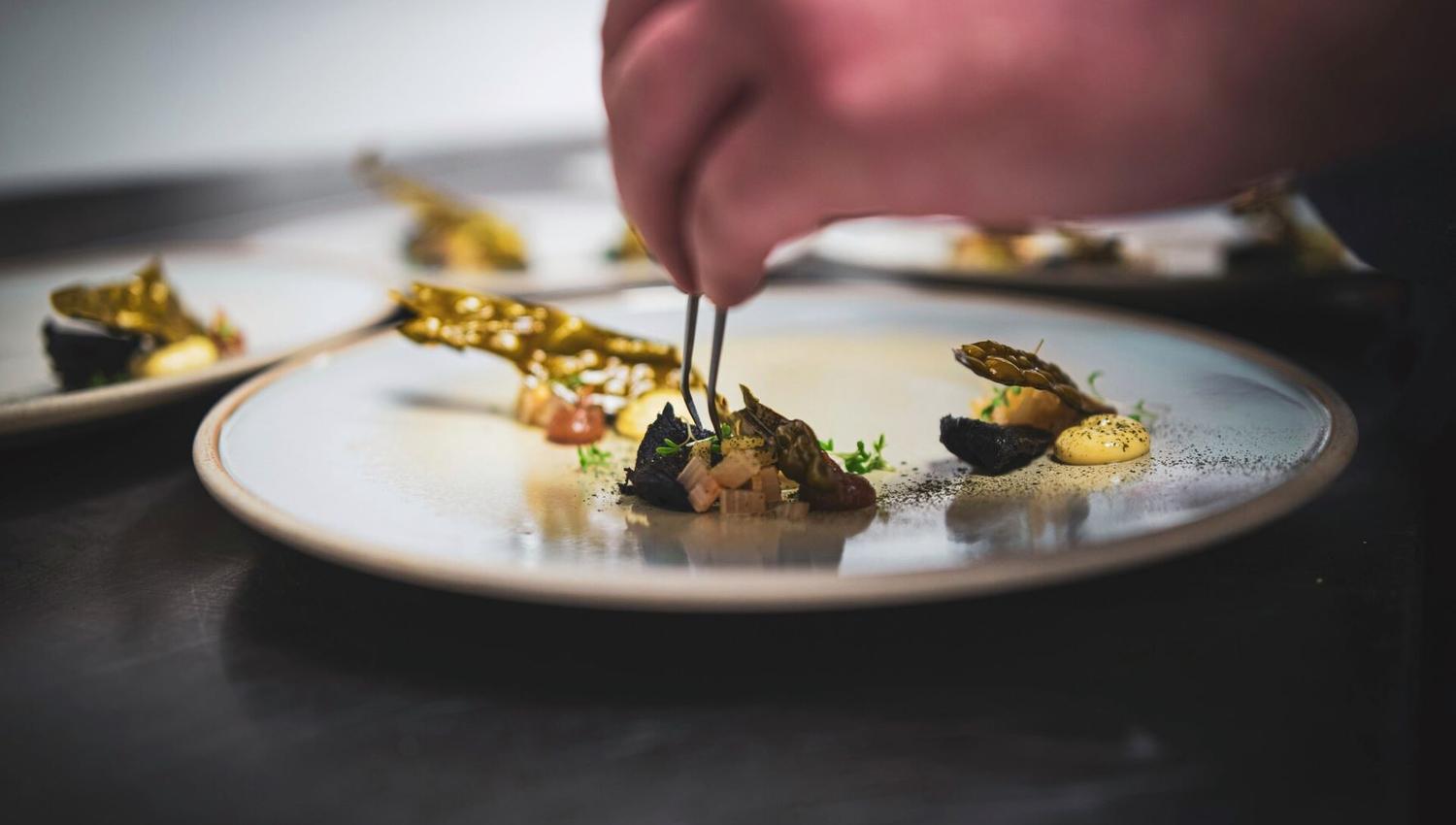 A chef preparing a dish on a plate with pincers