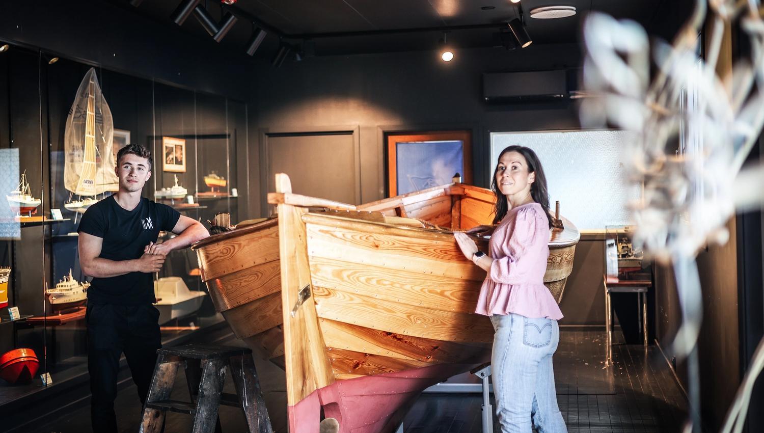A guide and a lady are looking at a wooden boat.