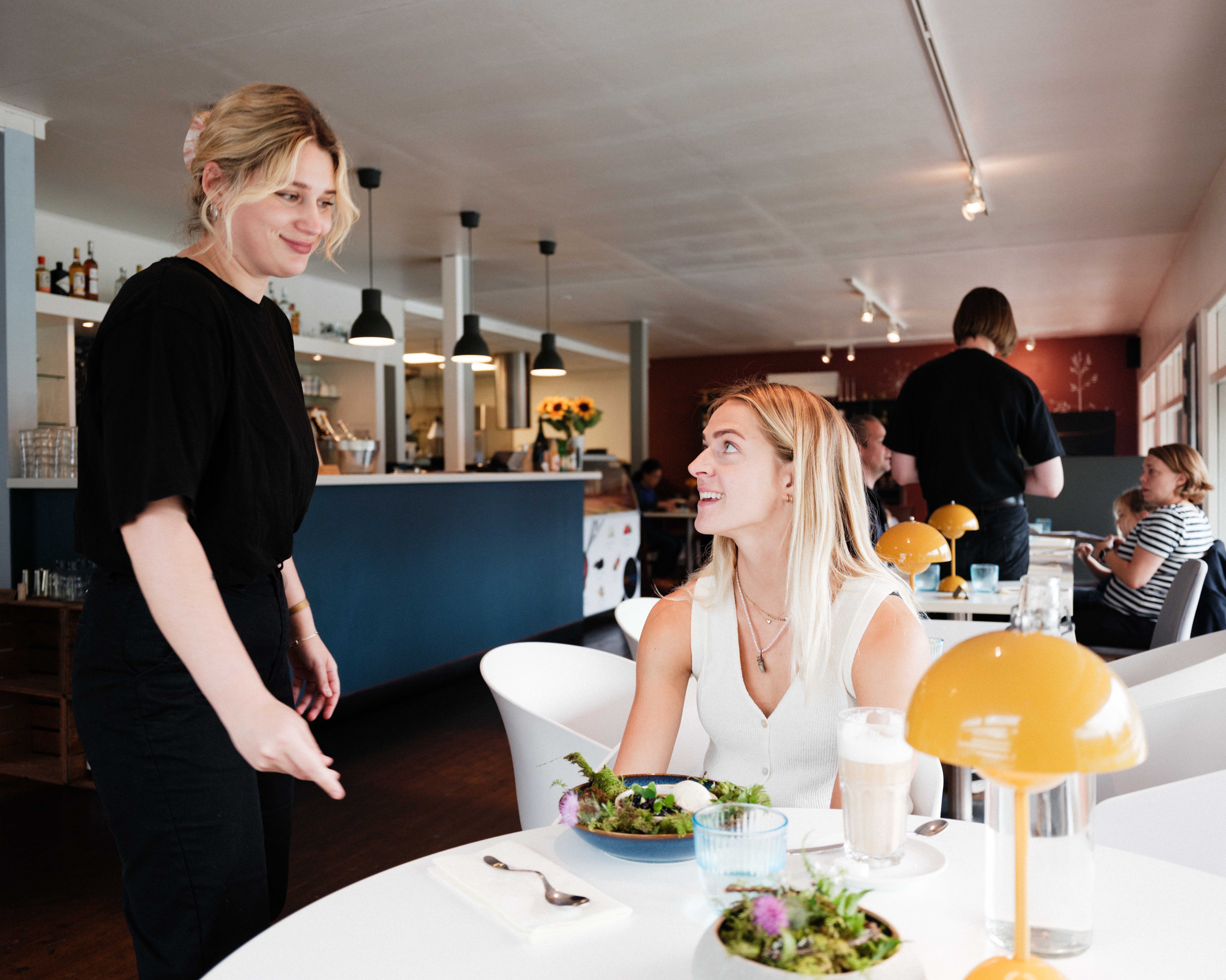 A waiter delivers a colourful and fresh dish to a smiling guest at Gløyp Spiseri.
