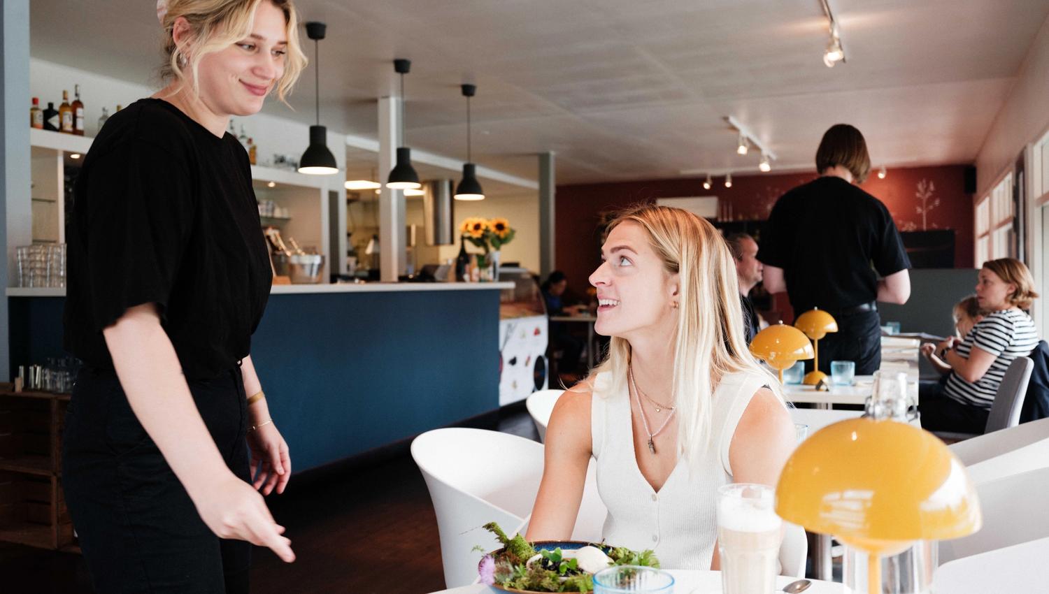 A waiter delivers a colourful and fresh dish to a smiling guest at Gløyp Spiseri.