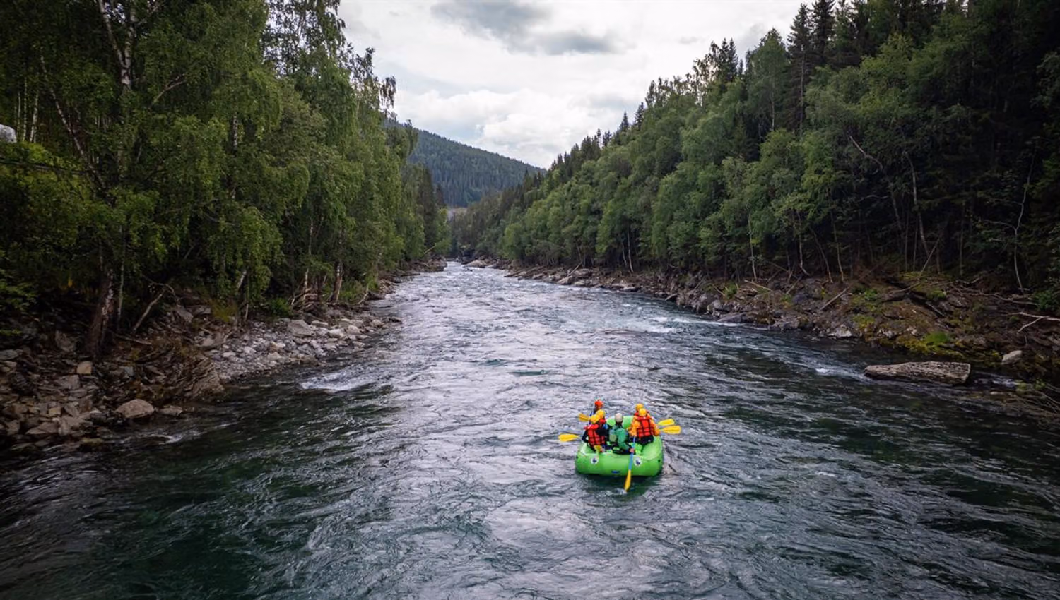Rafting boat moving through the current of the Sjoa River, with forested valley sides on both banks.