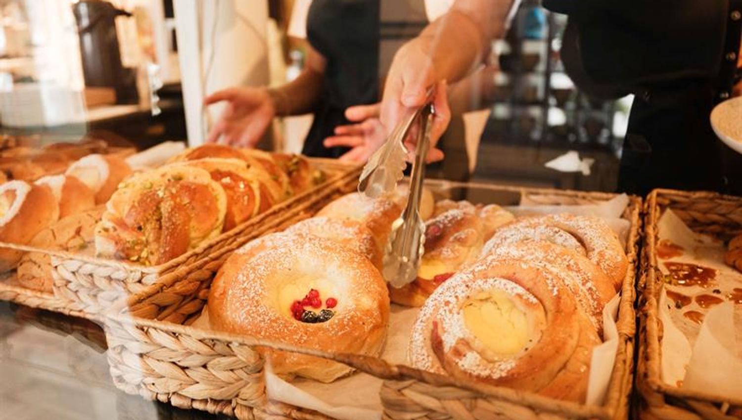 Freshly baked pastries are displayed in the counter inside Iversen Bakery and Gallery, while a staff member uses tongs to place baked goods behind the