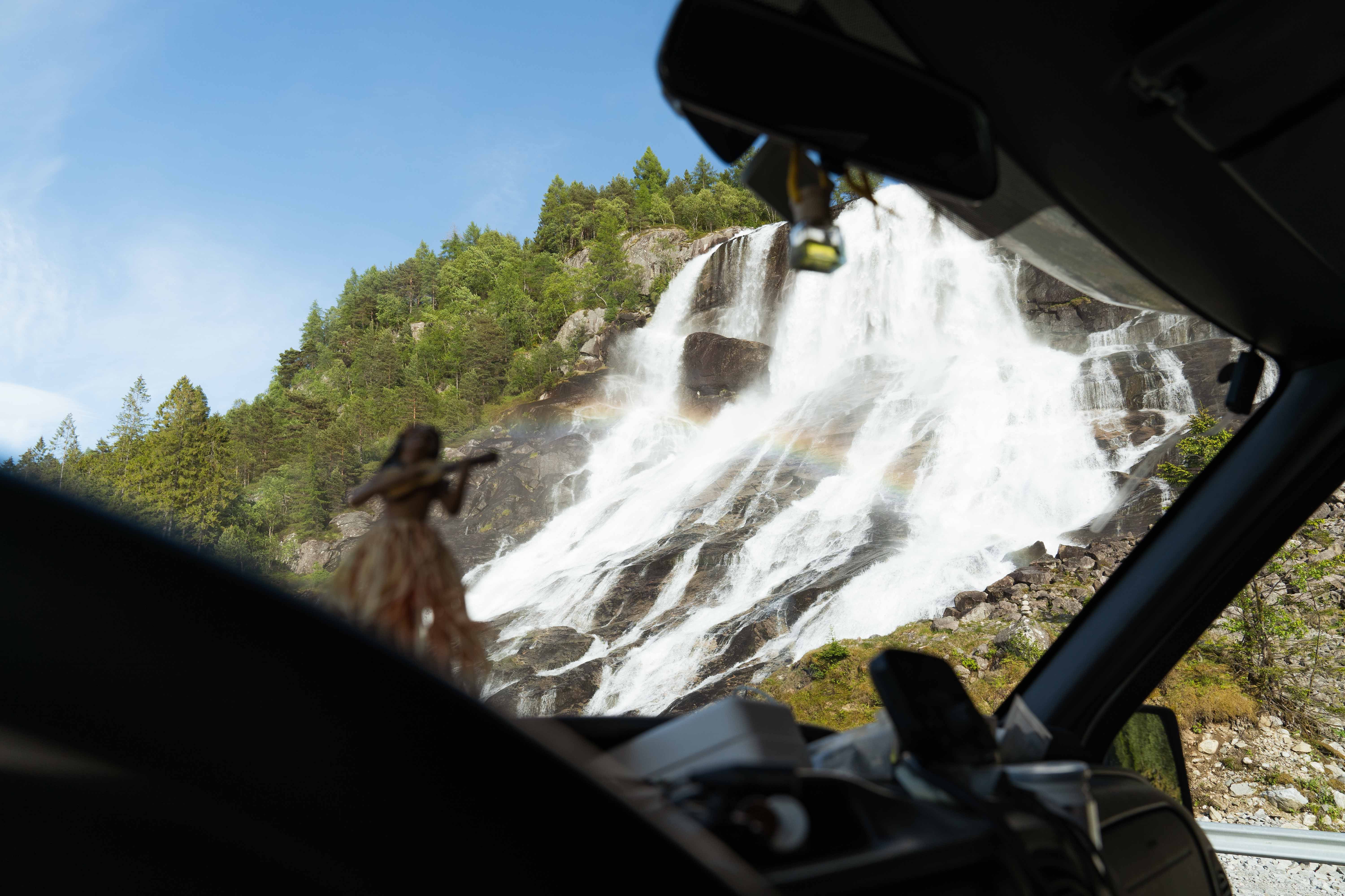 Furubergsfossen seen from the car – View of Furubergsfossen through the windshield, with a rainbow forming in the waterfall.
