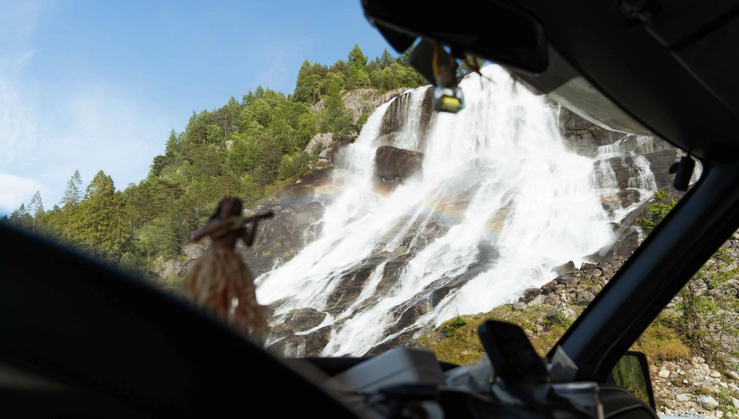 Furubergsfossen seen from the car – View of Furubergsfossen through the windshield, with a rainbow forming in the waterfall.