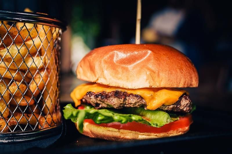 A burger served in a brioche bun with cheese, lettuce and tomato, accompanied by fries. The dish is part of the main menu.