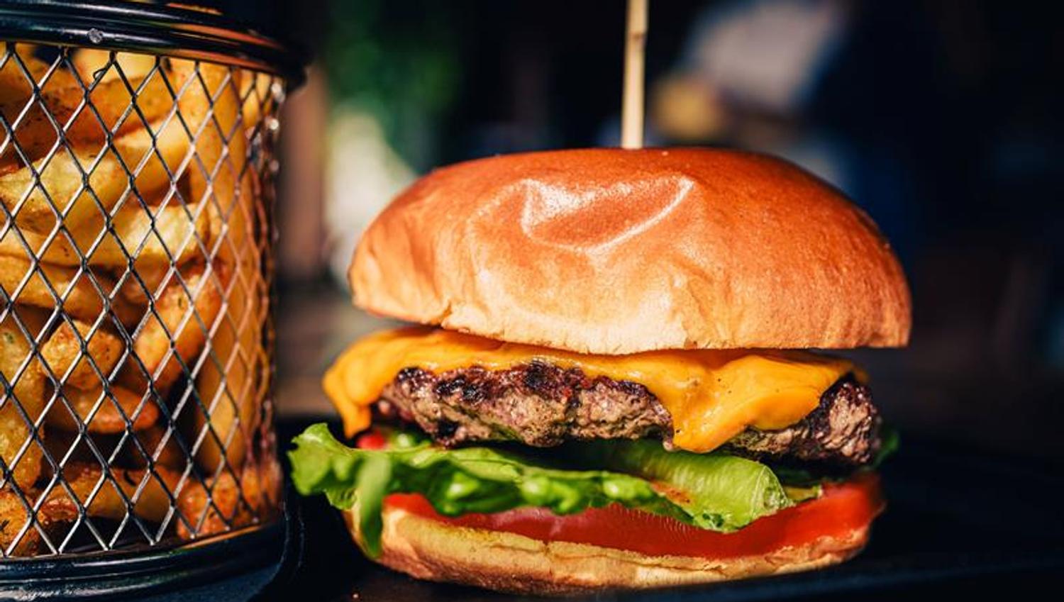 A burger served in a brioche bun with cheese, lettuce and tomato, accompanied by fries. The dish is part of the main menu.
