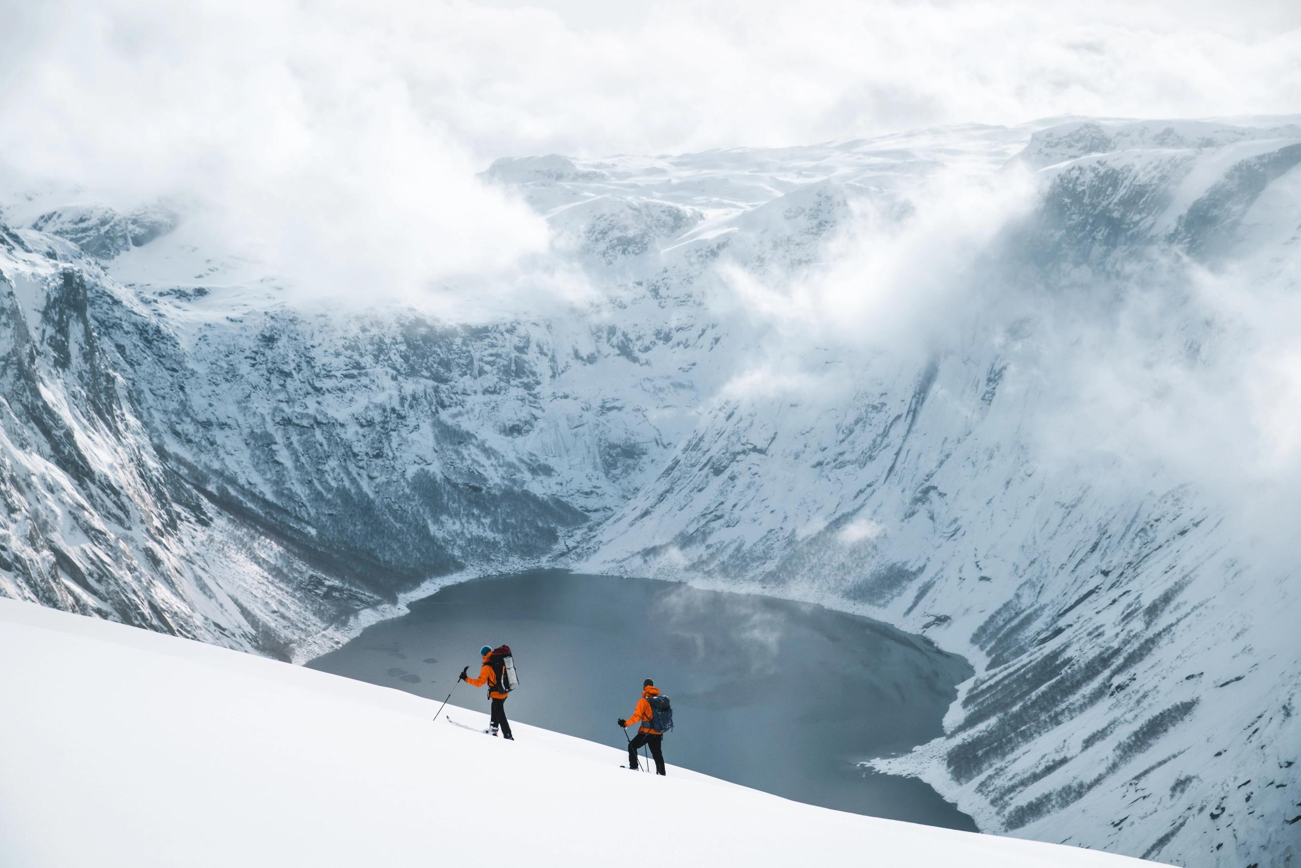 To skigåere ved et vann omringet av snøkledde fjell.