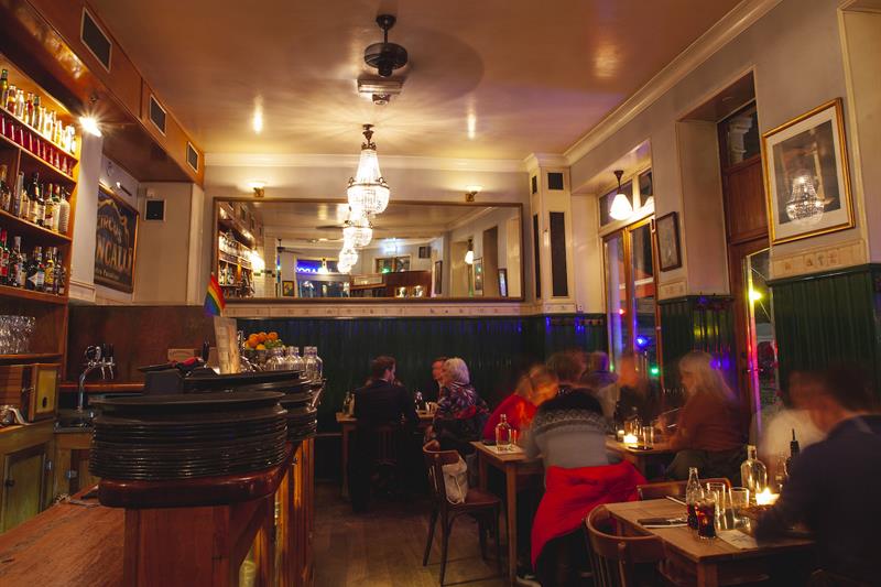 Restaurantinteriør med små spisebord og stoler, og lysekroner i taket