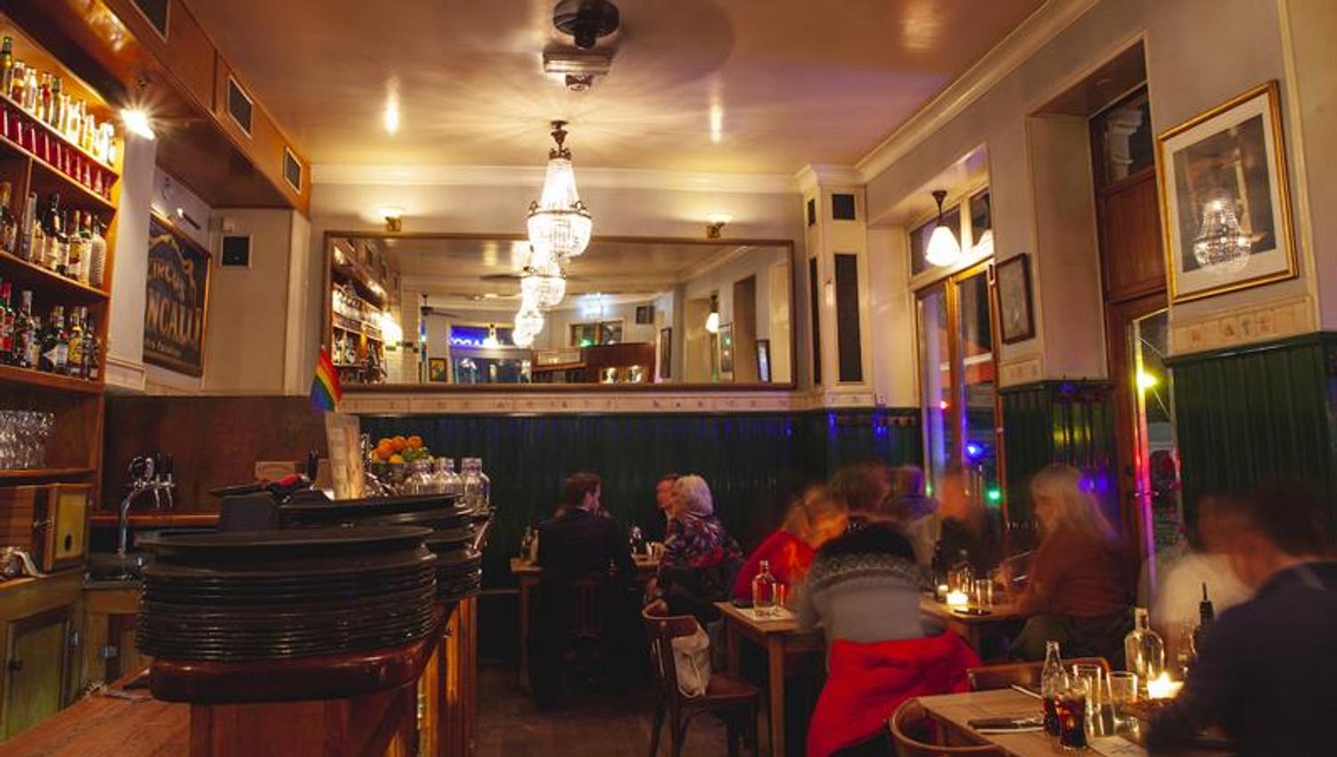 Restaurantinteriør med små spisebord og stoler, og lysekroner i taket