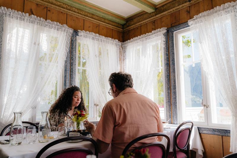 Guests dining in the wood-panelled dining room at Utne Hotel, with lace curtains and a glimpse of the fjord.