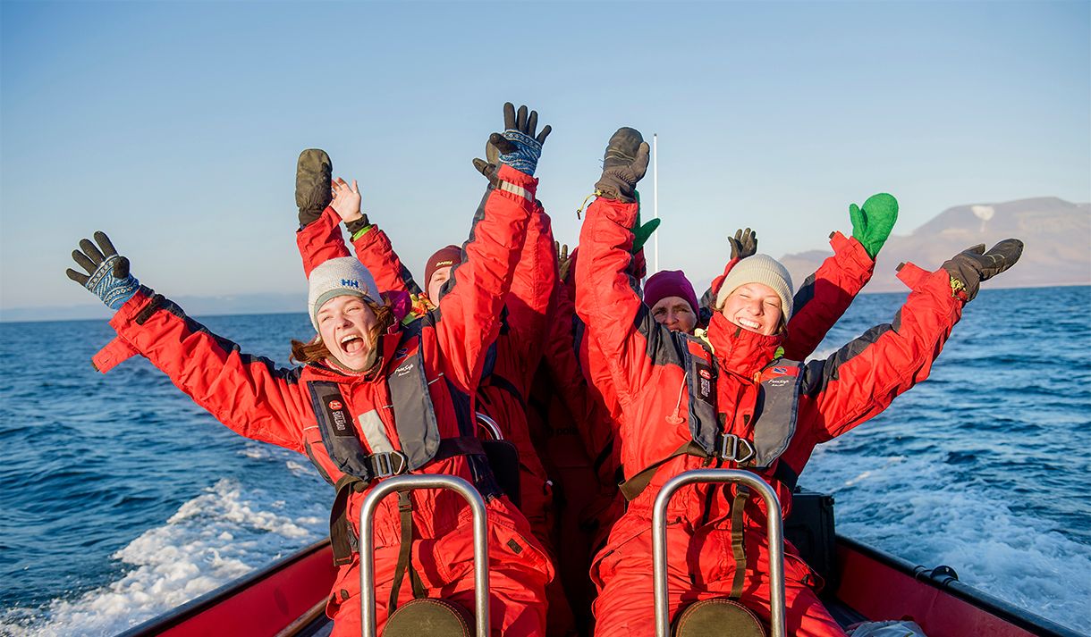 En gruppe gjester som sitter på en RIB båt i fart og jubler med hendene i været