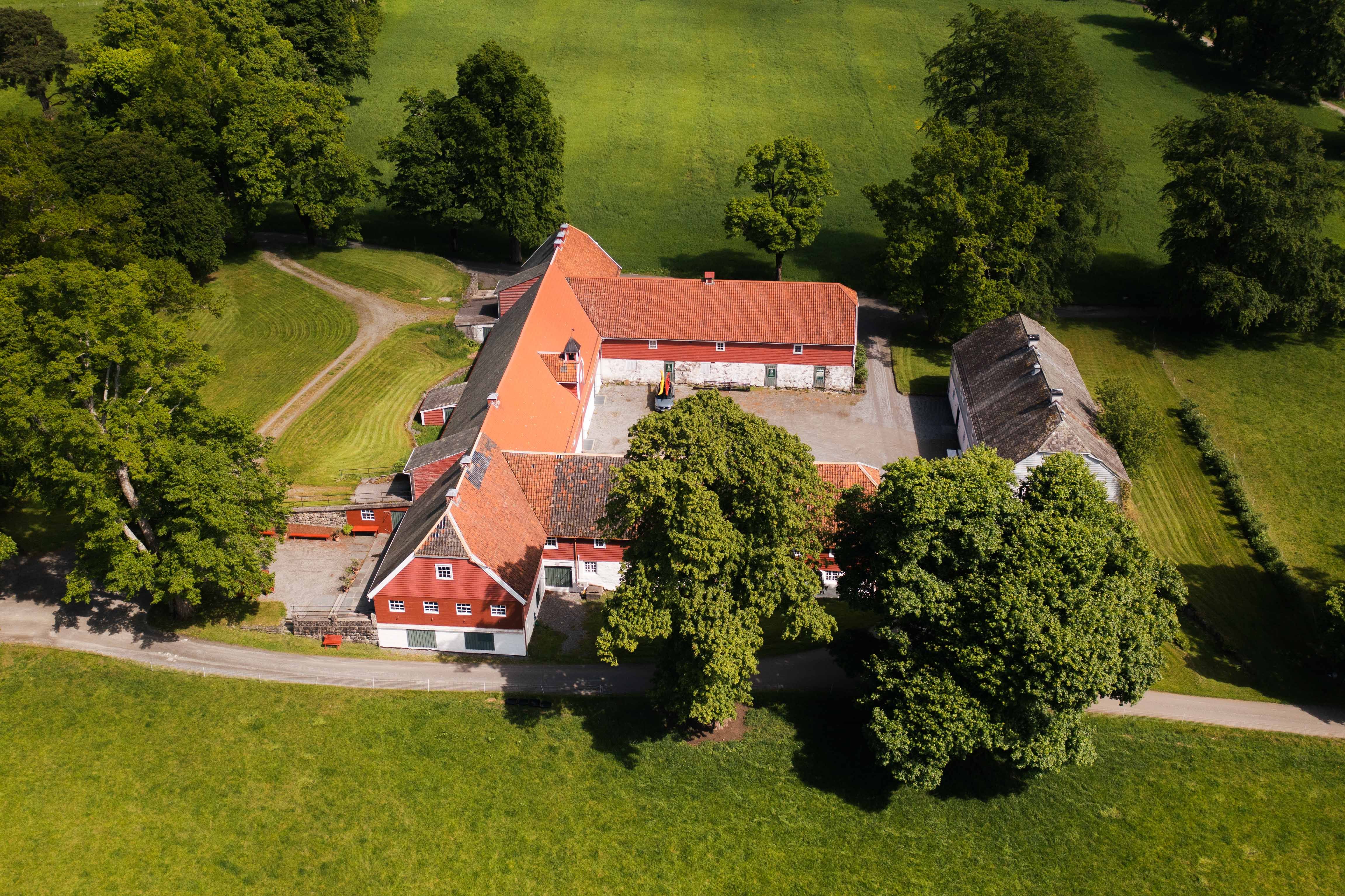 Nærbilete av Baroniet Rosendal Avlsgård – Det tradisjonsrike tunet sett frå lufta, med raudmåla bygningar og frodig landskap.