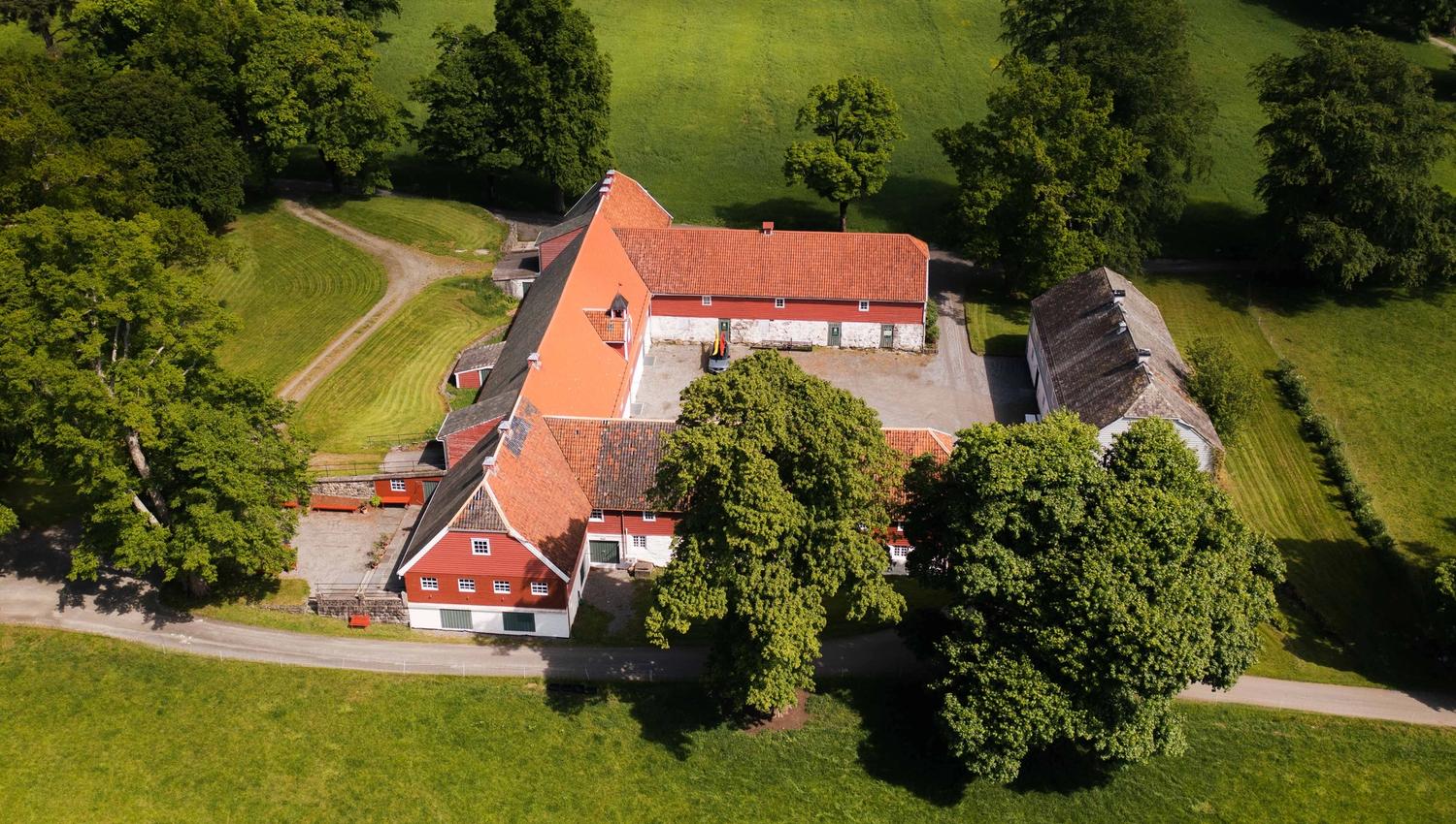 Nærbilete av Baroniet Rosendal Avlsgård – Det tradisjonsrike tunet sett frå lufta, med raudmåla bygningar og frodig landskap.