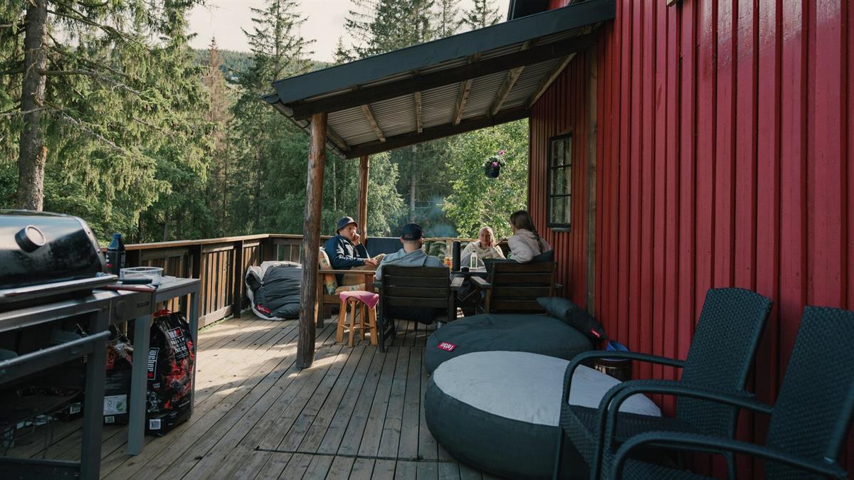 Terrasse ved en rød trebygning i skogsomgivelser, med sittegruppe og grill klart til bruk.