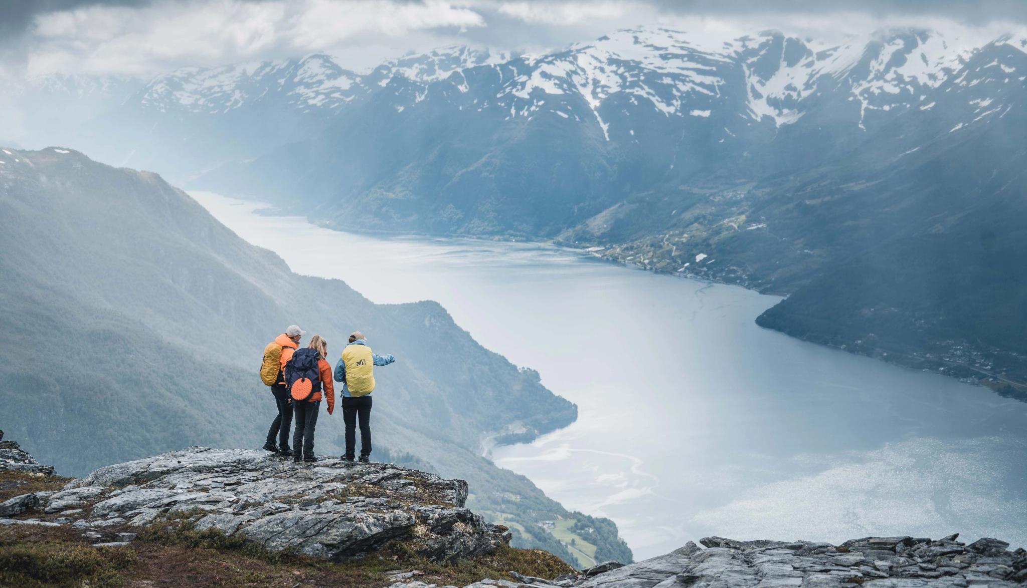Three hikers at the top of Dronningstien, enjoying a stunning view of Sørfjorden and Folgefonna glacier in the background.