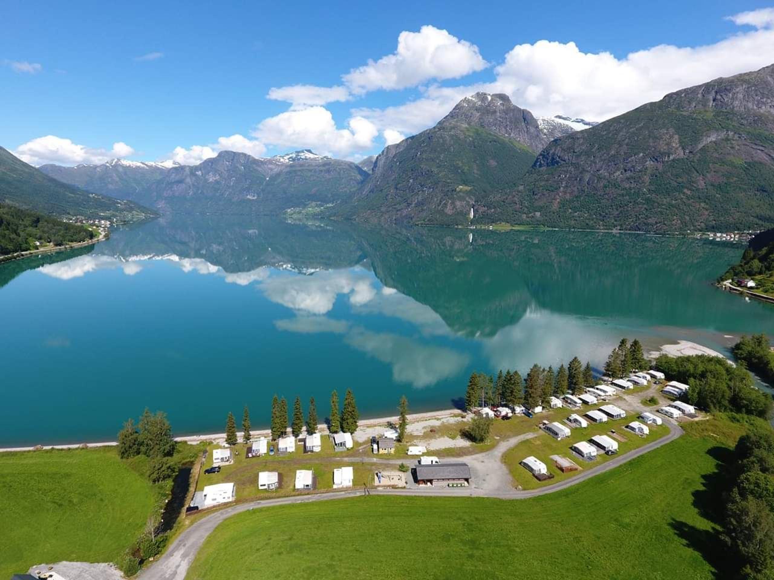 Droneutsikt over Grande Camping ved Oppstrynsvatnet i Oppstryn, omgitt av fjell og den blågrøne fargen frå brevatnet.