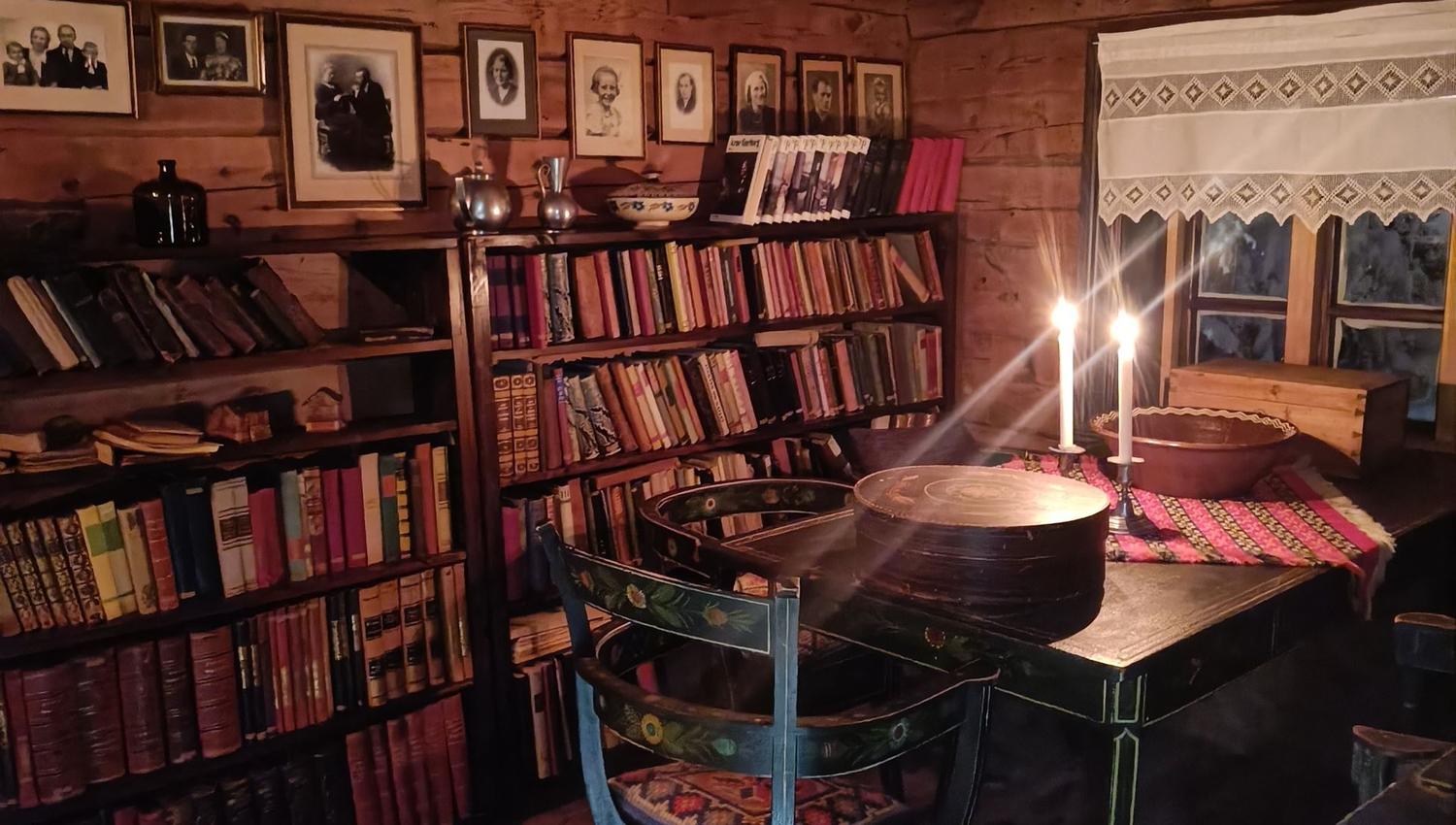 Orheimstunet in Nordfjord - Rustic wooden room with bookshelves, framed portraits, a table with two lit candles, and a window with a lace curtain..