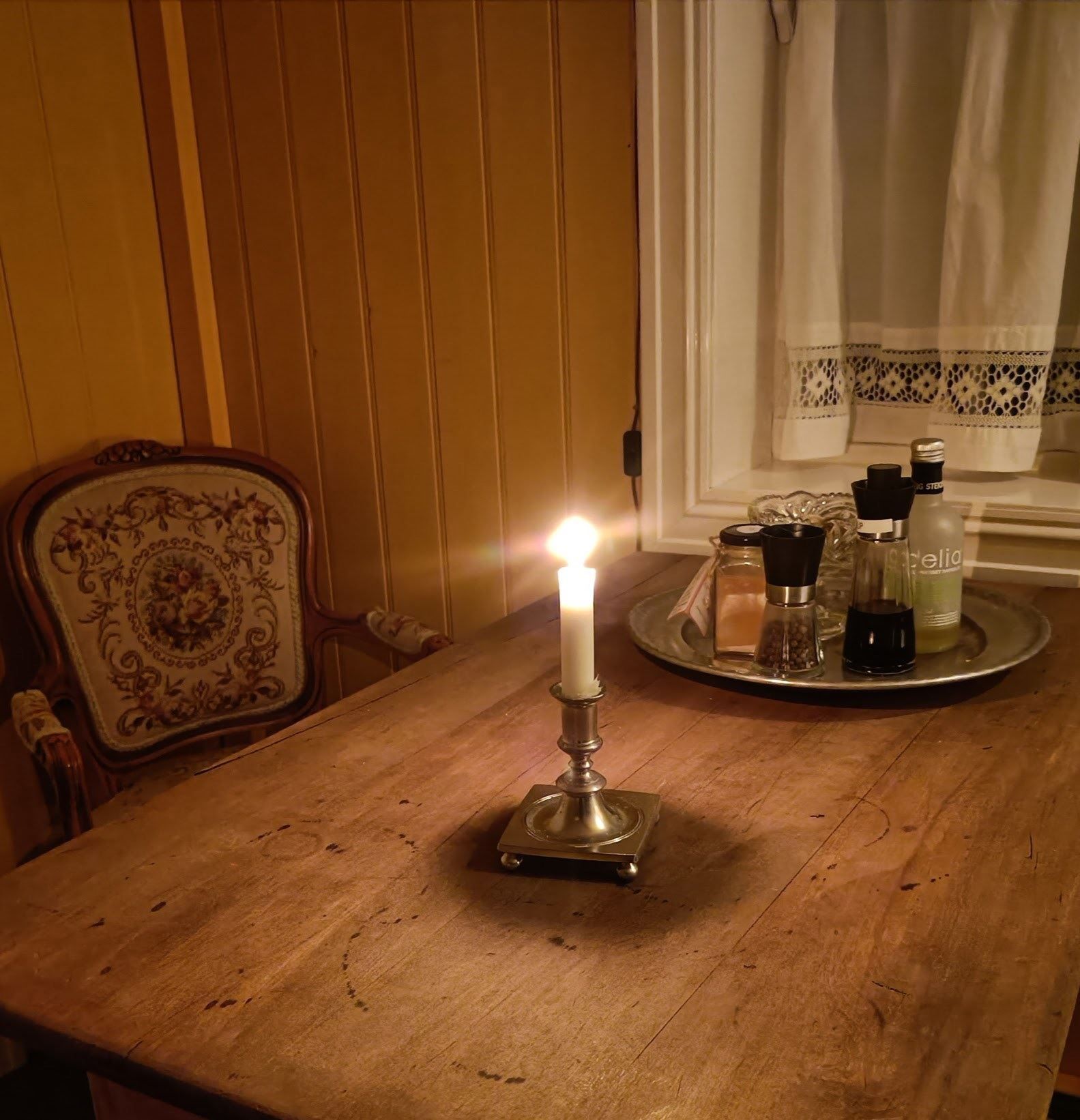 Orheimstunet in Nordfjord - A lit white candle in a brass holder sits on a wooden table beside a tray with spice grinders by a window..