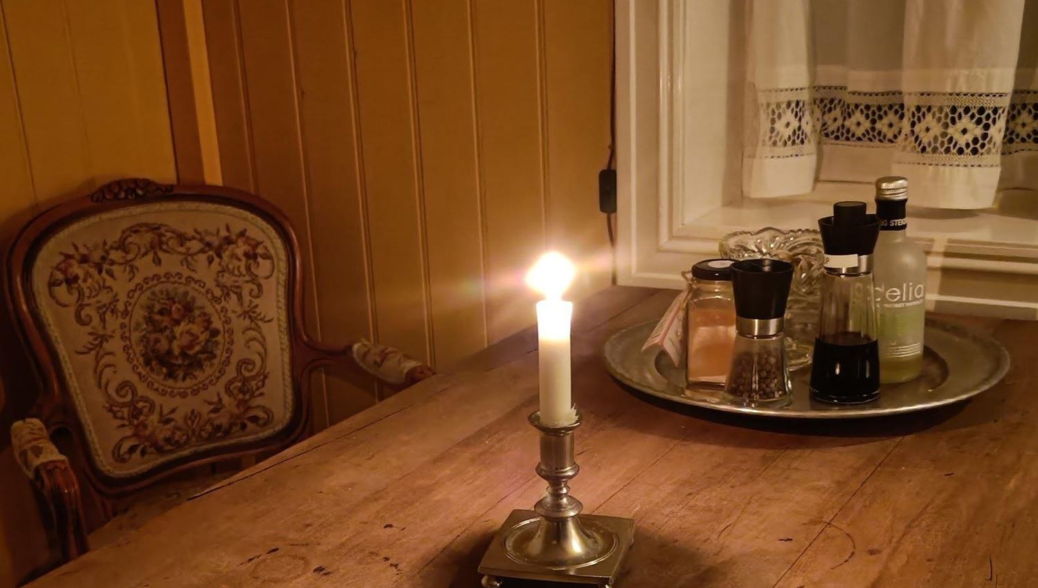 Orheimstunet in Nordfjord - A lit white candle in a brass holder sits on a wooden table beside a tray with spice grinders by a window..