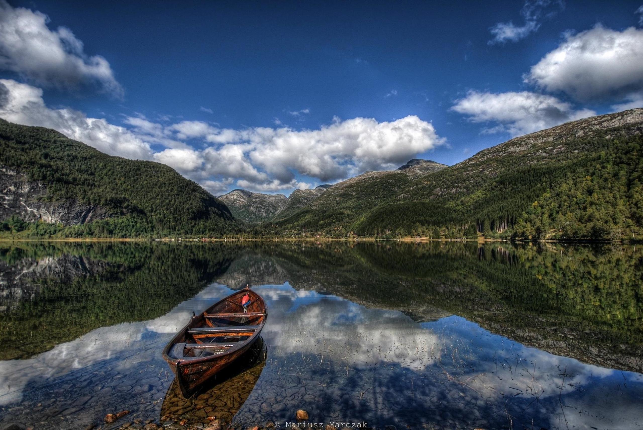 Quiet morning at Lake Fitjadalsvatnet in Hardanger, with a wooden rowboat and majestic mountains mirrored in the calm water.