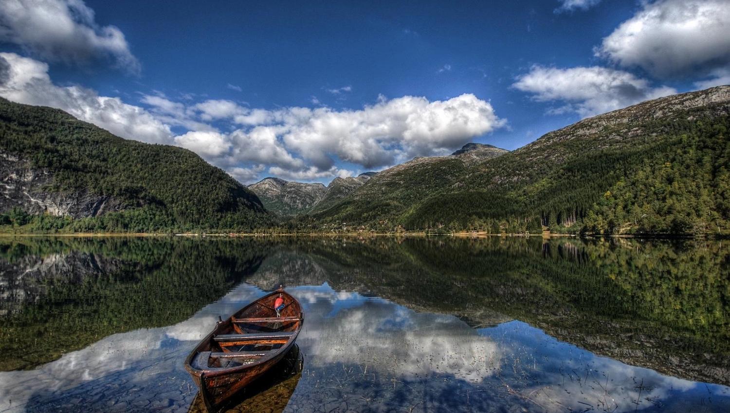 Quiet morning at Lake Fitjadalsvatnet in Hardanger, with a wooden rowboat and majestic mountains mirrored in the calm water.