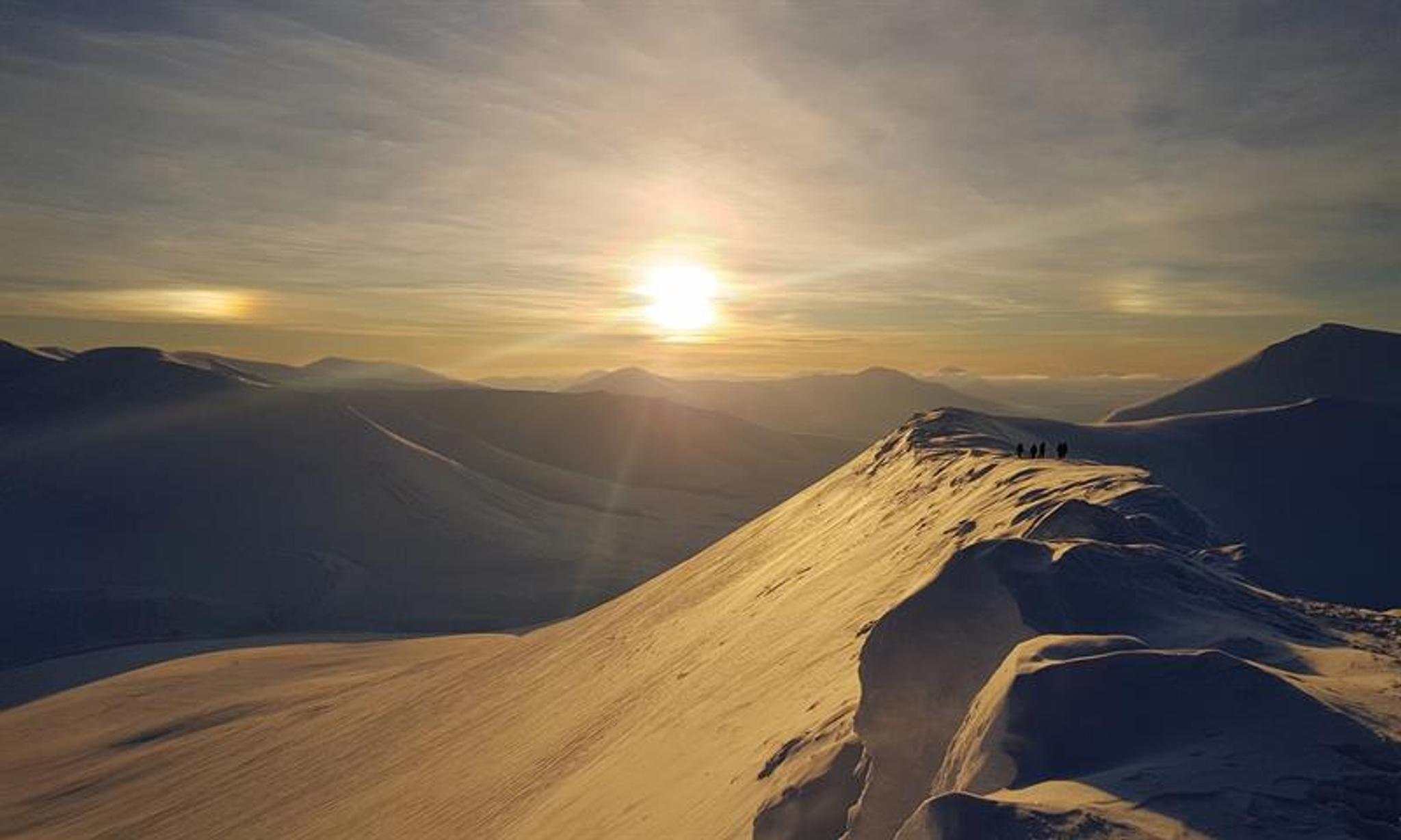 Sola som skinner på toppen av et snødekt fjell med nydelige fjell i bakgrunnen