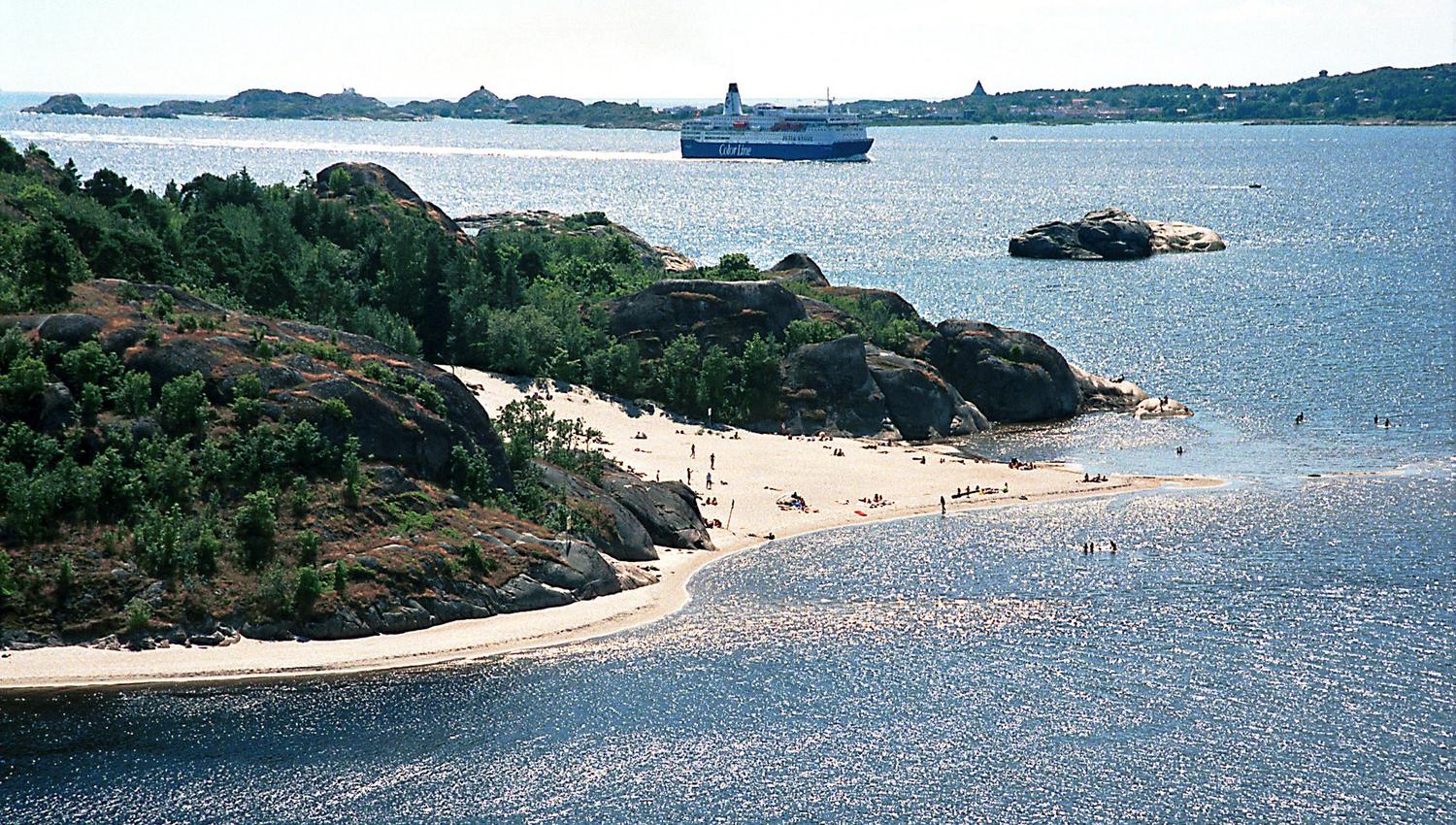 Hav, sandstrand og grønne trær på fjell
