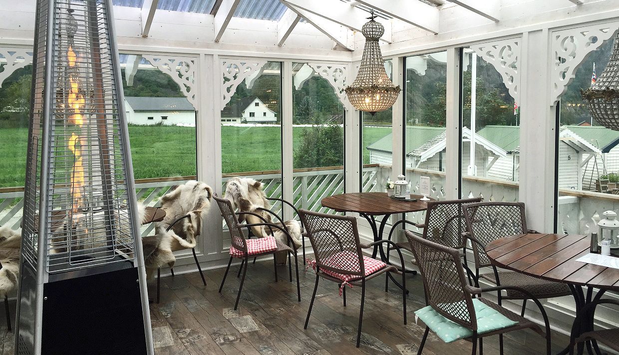 A dining terrace with tables and chairs, a terrace heater and chandelairs hanging from the ceiling.