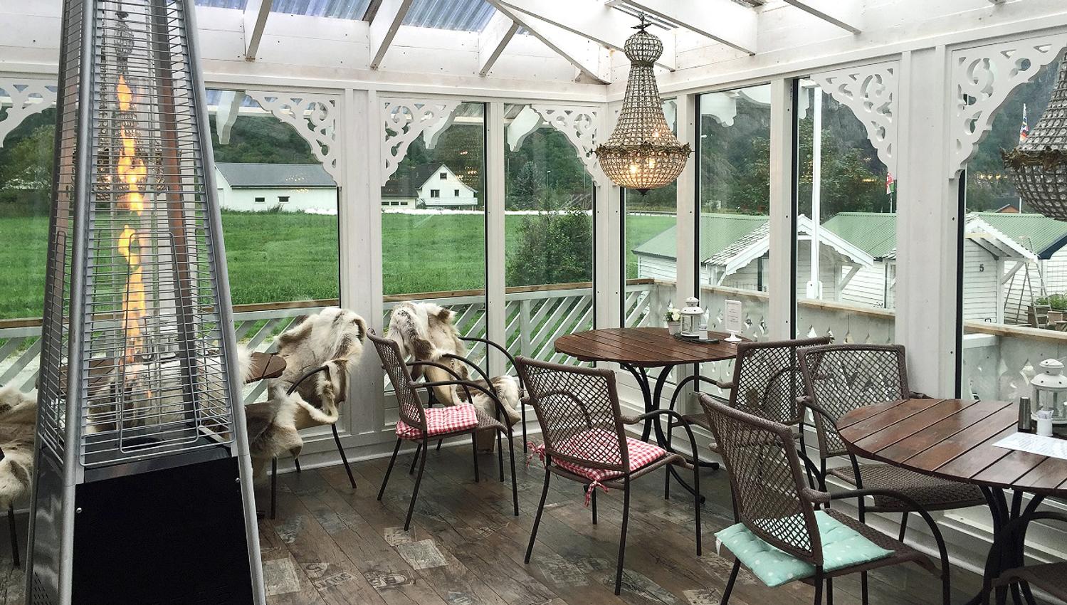 A dining terrace with tables and chairs, a terrace heater and chandelairs hanging from the ceiling.