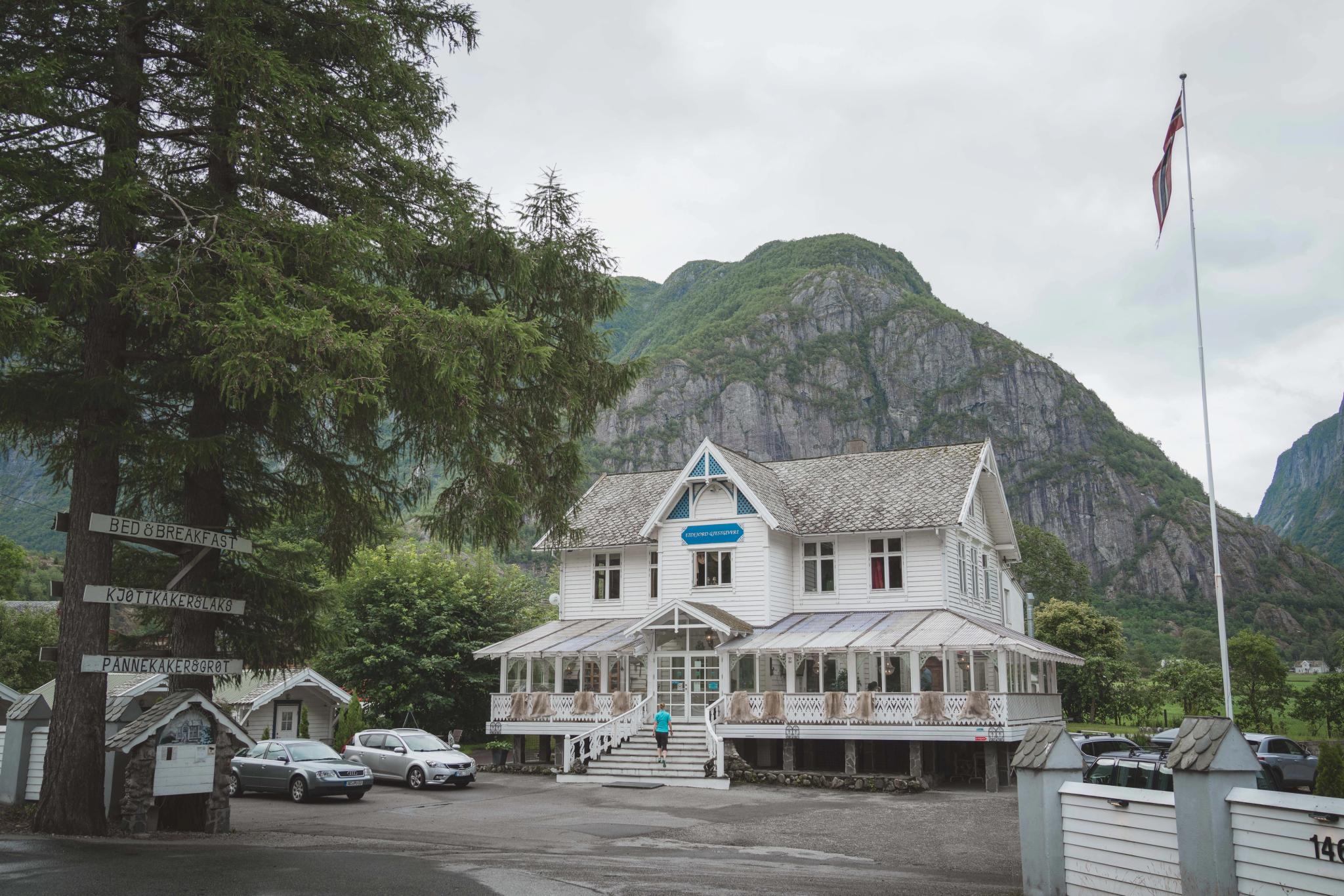 Showing Eidfjord Gjestgiveri from the outside. It's a large wooden house, white, with woodcarved details.