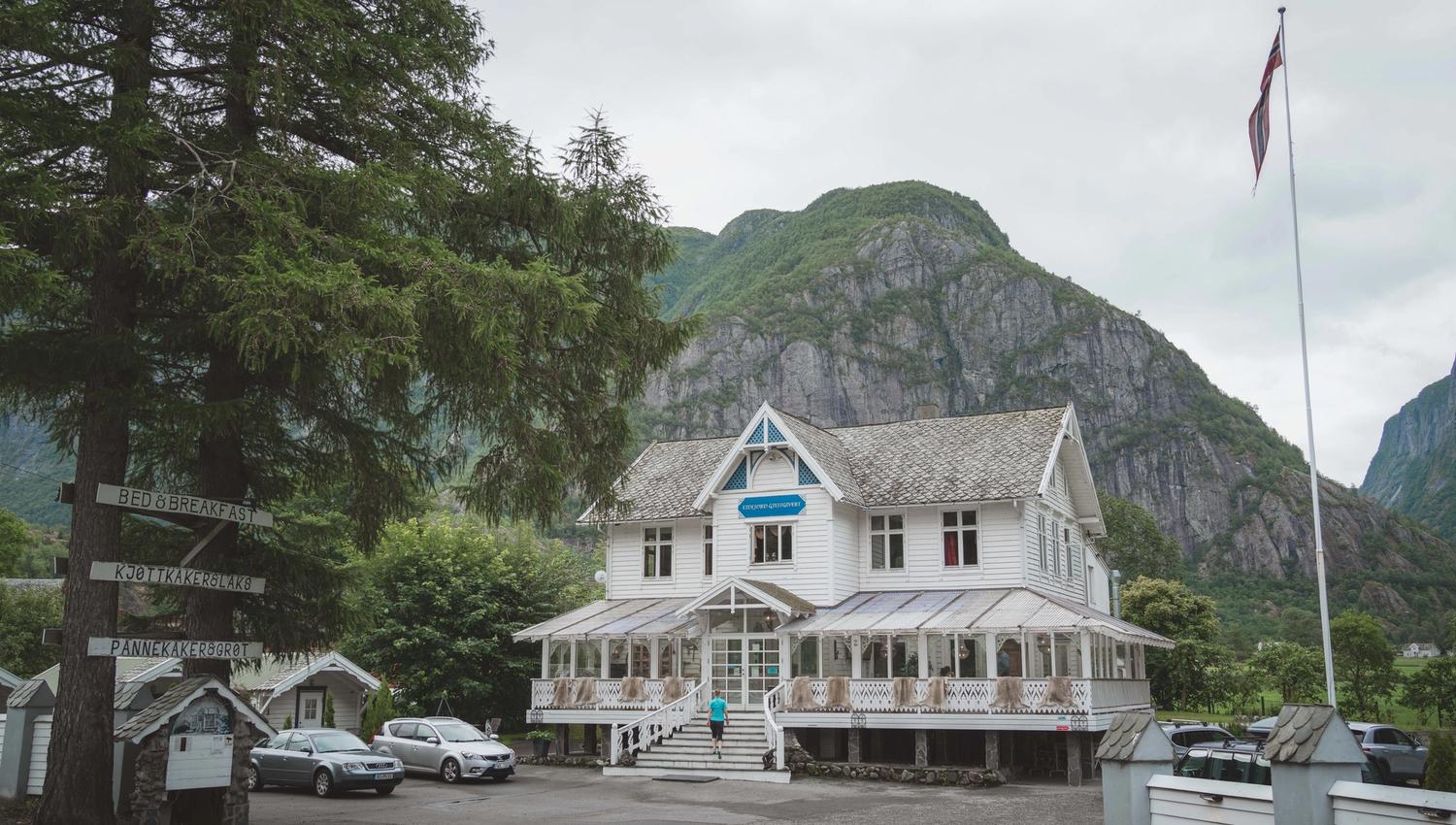 Showing Eidfjord Gjestgiveri from the outside. It's a large wooden house, white, with woodcarved details.