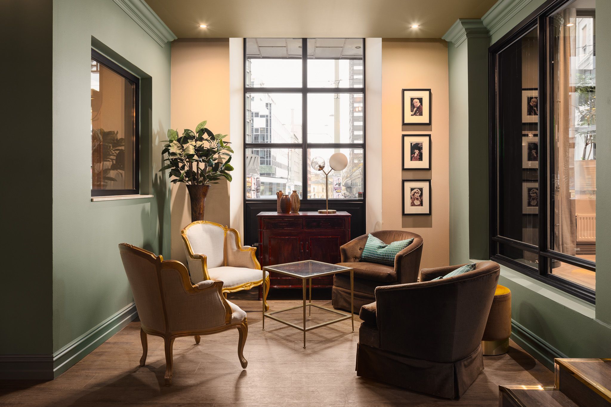 A lounge with armchairs, a potted plant in the corner, and windows
