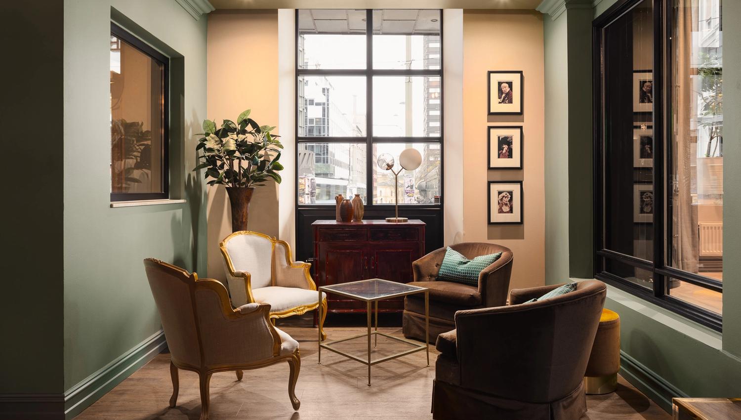 A lounge with armchairs, a potted plant in the corner, and windows