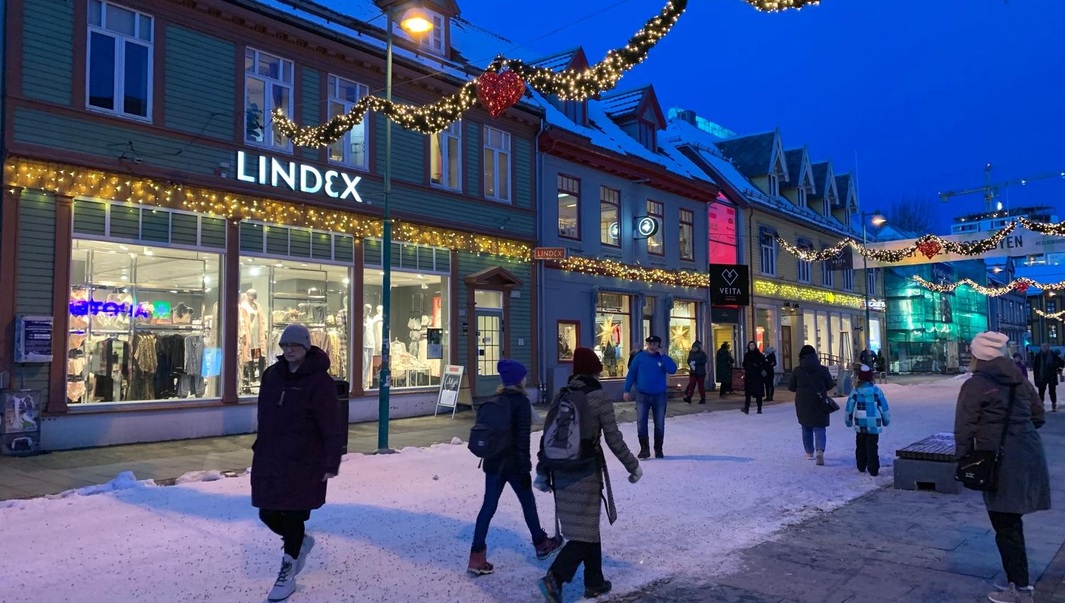 Folk går i snødekt gate med julelys og butikker en vinterkveld